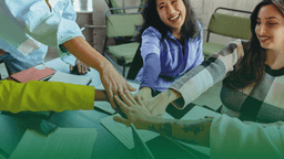 Grupo de colaboradores com mãos unidas sobre a mesa, sorrindo, simbolizando união, diversidade e colaboração no ambiente corporativo.
