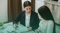 Duas mulheres sentadas em uma mesa analisam documentos durante um processo seletivo, representando a exigência de antecedentes criminais como parte da contratação.