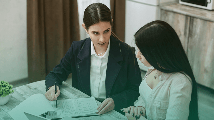 Duas mulheres sentadas em uma mesa analisam documentos durante um processo seletivo, representando a exigência de antecedentes criminais como parte da contratação.