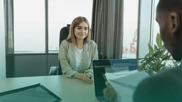 Entrevista de emprego com recrutador verificando currículo enquanto candidata aguarda avaliação, ilustrando a importância da verificação de dados profissionais.