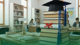 Pilha de livros acadêmicos sobre mesa em uma sala de estudos. No topo da pilha, um chapéu de formatura. No meio dos livros, um diploma enrolado com um laço de fita vermelha. Ao fundo, estudantes e estantes de livros.